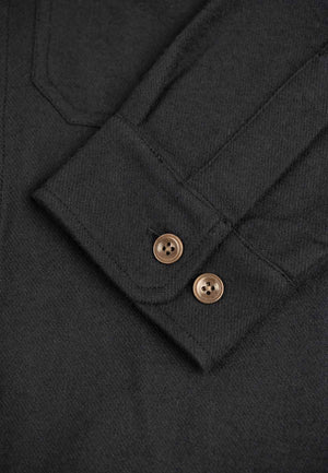 Close up of the buttoned sleeve of a black flannel shirt.