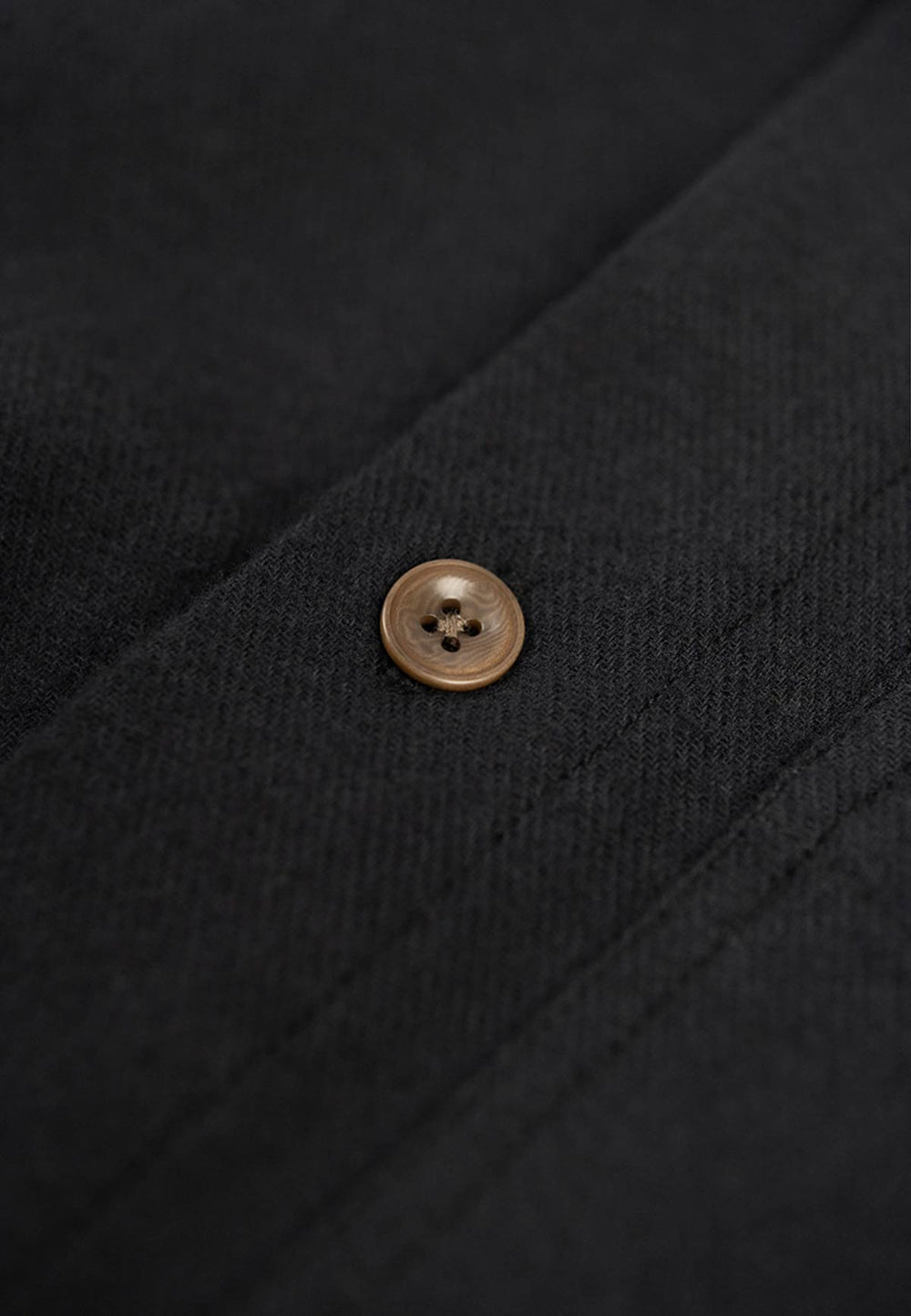 Close up of the button closure of a black flannell shirt.