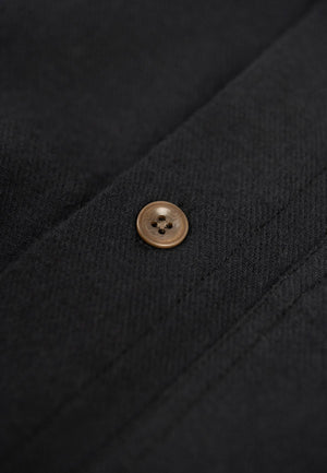 Close up of the button closure of a black flannell shirt.